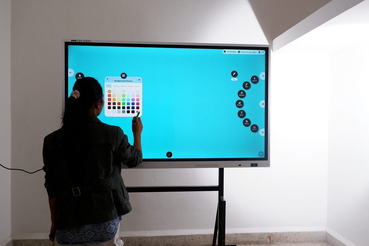 nauczyciel w koszuli dotyka ekranu tablicy interaktywnej przed grupą uczniów w klasie