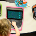 uczeń szkolny pracujący na laptopie przy biurku w jasnym pokoju studyjnym z otwartymi podręcznikami