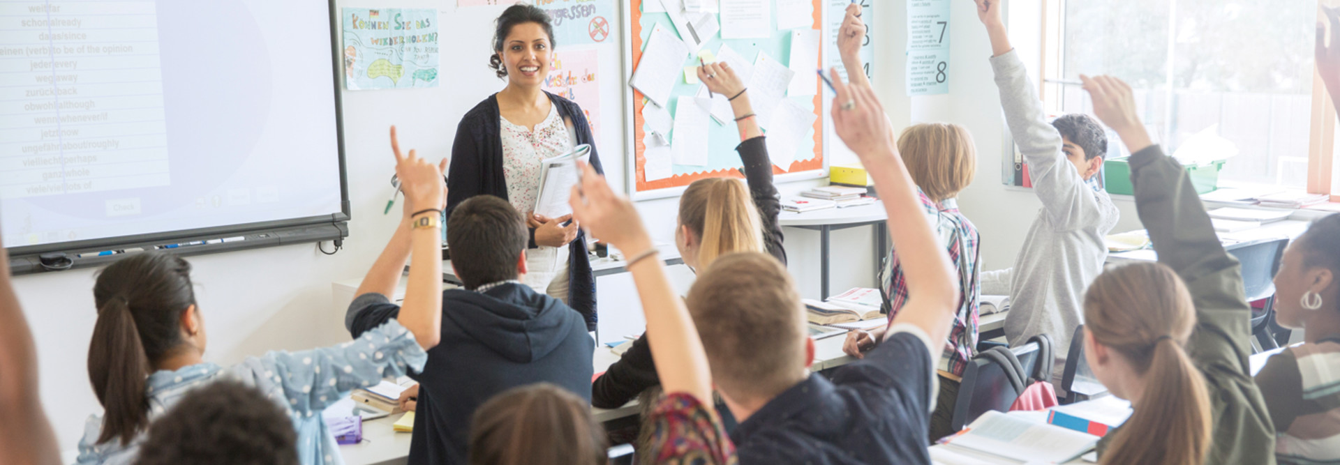 Dziecko stoi przed klasą z pilotem i wskazuje na swój slajd na ścianie
