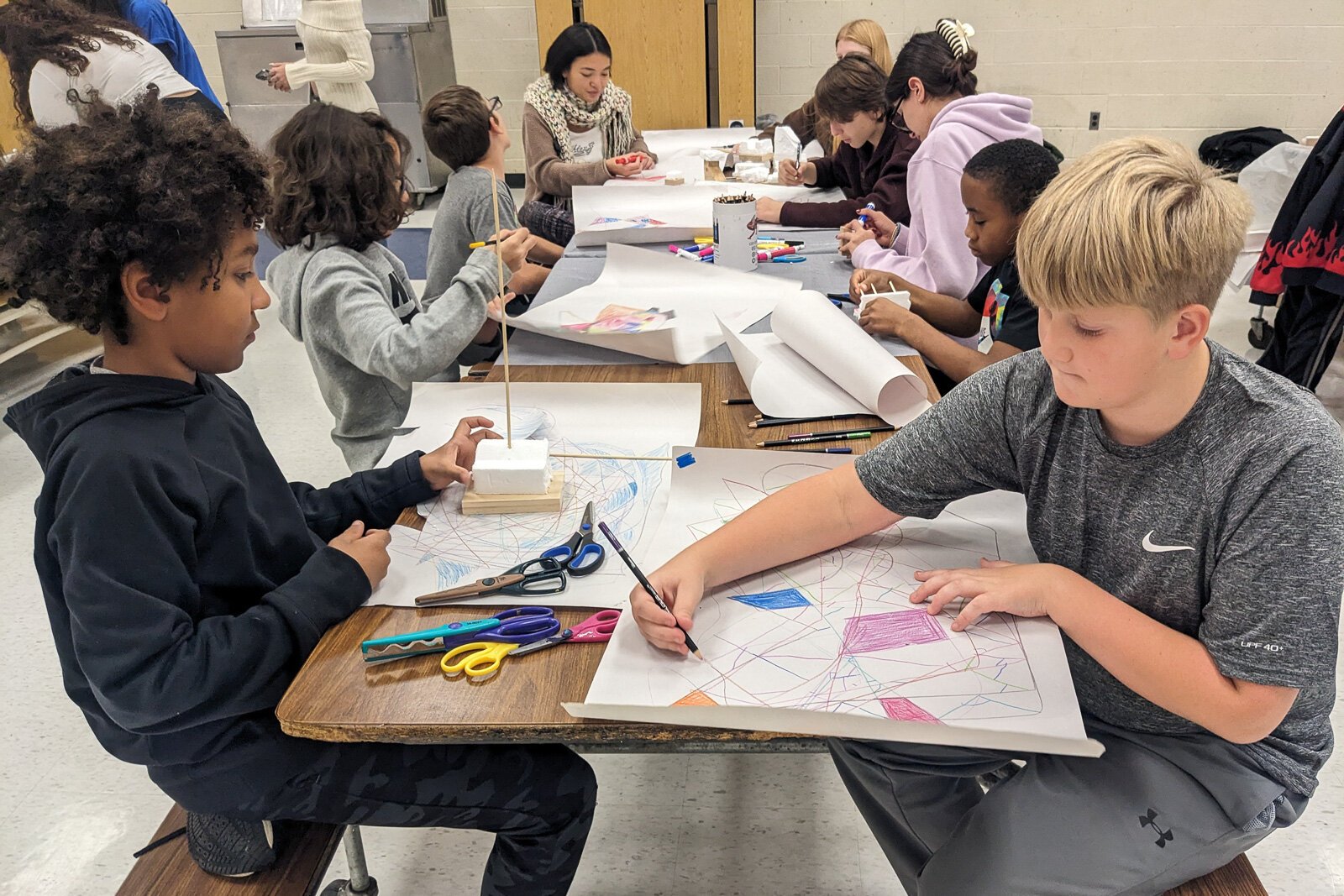 czterech uczniów dyskutuje pomysły przy stole z rysunkami i zdjęciami