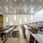 jasno oświetlona sala lekcyjna z uczniami przy ławkach i nauczycielem przy tablicy