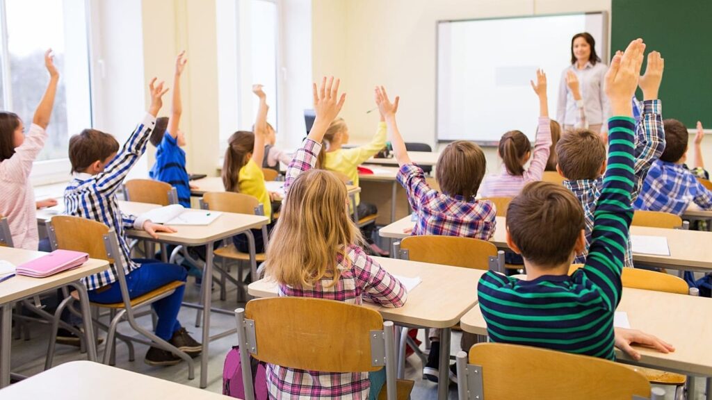 uśmiechnięte dzieci w jasnej klasie fińskiej szkoły siedzą w kręgu na podłodze