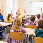 uśmiechnięte dzieci w jasnej klasie fińskiej szkoły siedzą w kręgu na podłodze