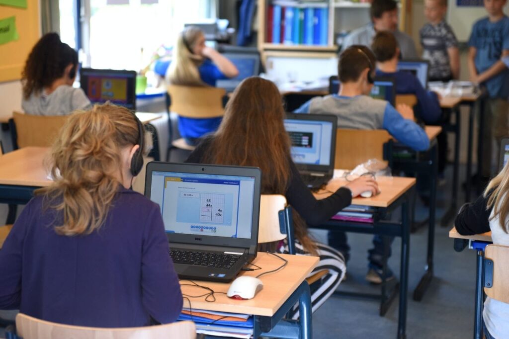 grupa uczniów i nauczyciel w sali z laptopami i interaktywną tablicą