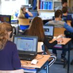 grupa uczniów i nauczyciel w sali z laptopami i interaktywną tablicą